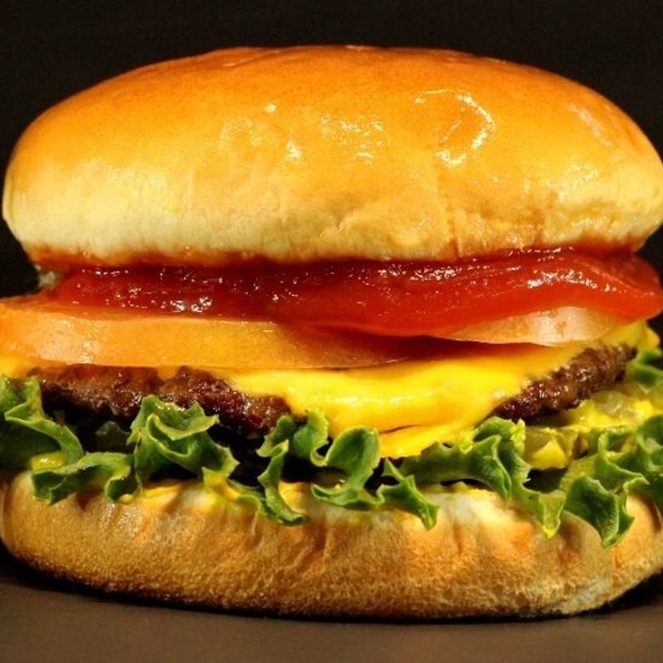 A classic cheeseburger with lettuce, tomato, and ketchup on a toasted bun against a dark background.