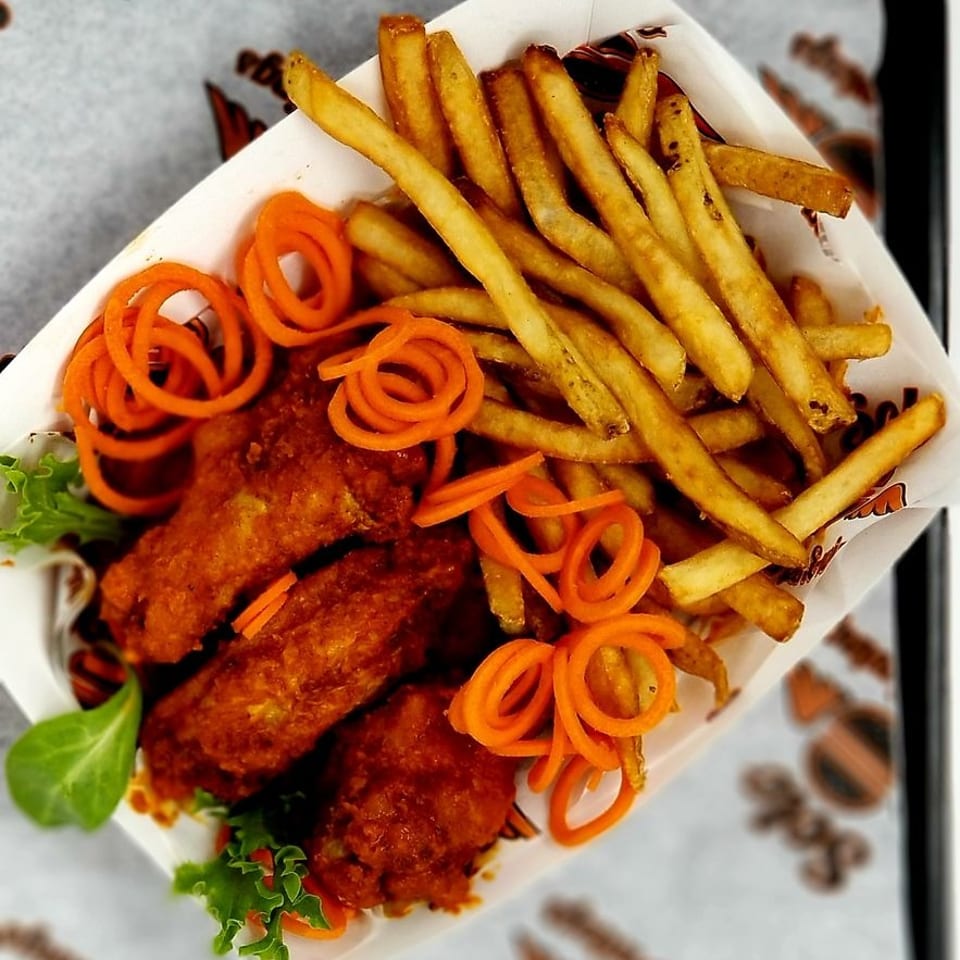 Crispy chicken wings, golden fries, and carrot spirals in a white paper tray.